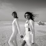 Diverse women in stylish outfits holding hands in desert